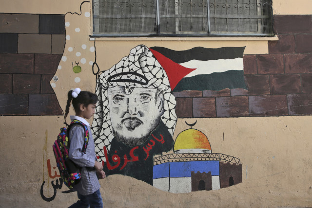 A child walks in front of a mural painting depicting the late Palestinian leader Yasser Arafat on her way to a school run by United Nations Agency for Palestinian Refugees (UNRWA) in Balata refugee camp, east of Nablus on August 29, 2018 (credit: JAAFAR ASHTIYEH / AFP)