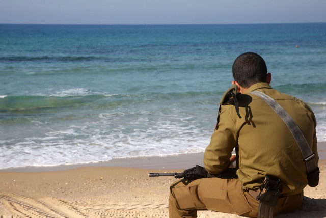 An IDF soldier sits on a beach in Tel Aviv (credit: MARC ISRAEL SELLEM/THE JERUSALEM POST)