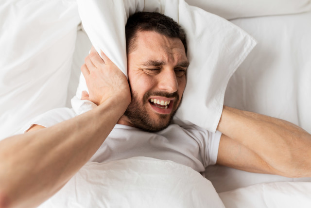Man lying in bed with pillow suffering from noise  (credit: INGIMAGE)