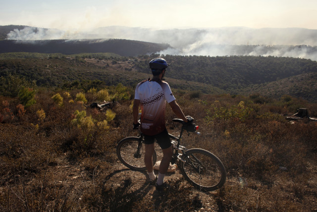 A man stands next to his bicycle as he looks at a forest fire on Mount Carmel, near the northern city of Haifa December 3, 2010. International firefighting teams were on Friday helping Israel battle a huge forest fire close to the port city of Haifa that has killed at least 42 people and forced mass (credit: REUTERS/NIR ELIAS)