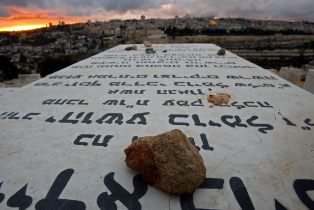 Stones placed in remembrance lie on grave tablets on the Mount of Olives Jewish cemetary as the sun sets in Jerusalem (credit: LASZLO BALOGH/ REUTERS)