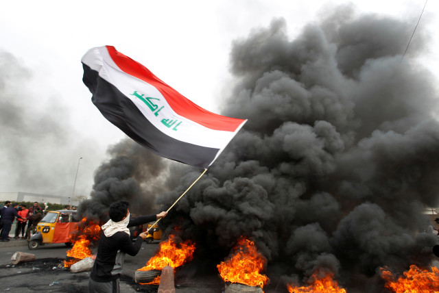 A demonstrator carries an Iraqi flag as he walks near burning tires blocking a road during ongoing anti-government protests, in Baghdad, Iraq January 19, 2020. (credit: KHALID AL MOUSILY / REUTERS)