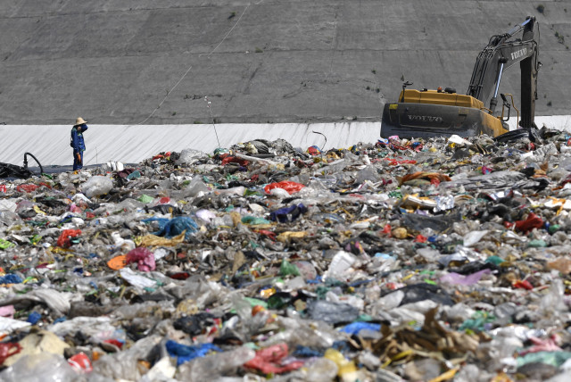 An environmental worker stands near an excavator amid waste at Tianziling landfill in Hangzhou, Zhejiang province, China August 7, 2019. (credit: REUTERS/STRINGER)