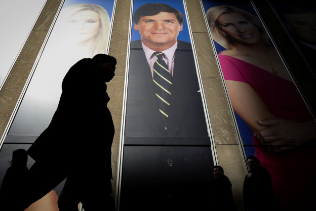 People pass by a promo of Fox News host Tucker Carlson on the News Corporation building in New York, U.S., March 13, 2019 (credit: REUTERS/BRENDAN MCDERMID)
