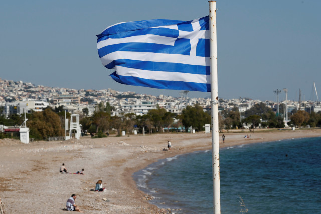 A Greek national flag flutters as people visit a beach, following the coronavirus disease (COVID-19) outbreak, in Athens, Greece, April 28, 2020. (credit: GORAN TOMASEVIC/REUTERS)