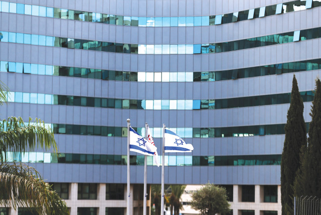 Israeli national flags flutter in front of an office tower at a business park housing high tech companies, at Ofer Park in Petah Tikva. (credit: RONEN ZVULUN / REUTERS)