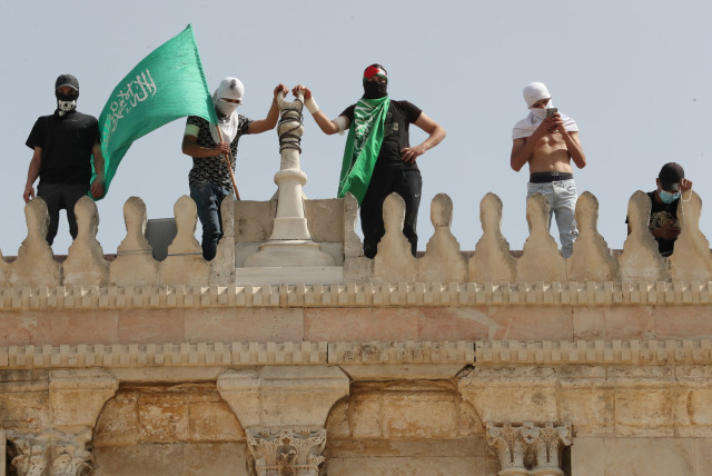 A Palestinian holds a Hamas flag as he stands next to others atop a walk of the al-Aqsa mosque following clashes with Israeli police at the compound that houses al-Aqsa Mosque, known to Muslims as Noble Sanctuary and to Jews as Temple Mount, in Jerusalem's Old City May 10, 2021. (credit: AMMAR AWAD/REUTERS)