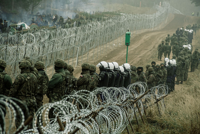  Polish soldiers and police watch migrants at the Poland/Belarus border near Kuznica, Poland, in this photograph released by the Territorial Defence Forces, November 12, 2021.  (credit: IREK DOROZANSKI/DWOT/HANDOUT VIA REUTERS)