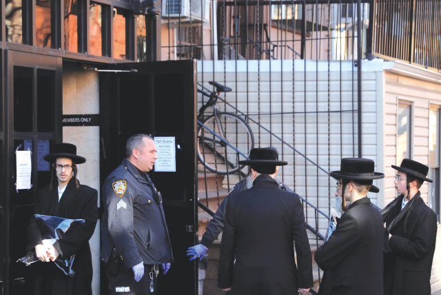 New York City police officers block hassidic men from entering a synagogue, closed due to COVID-19, in Brooklyn, in March 2020. (credit: ANDREW KELLY / REUTERS)