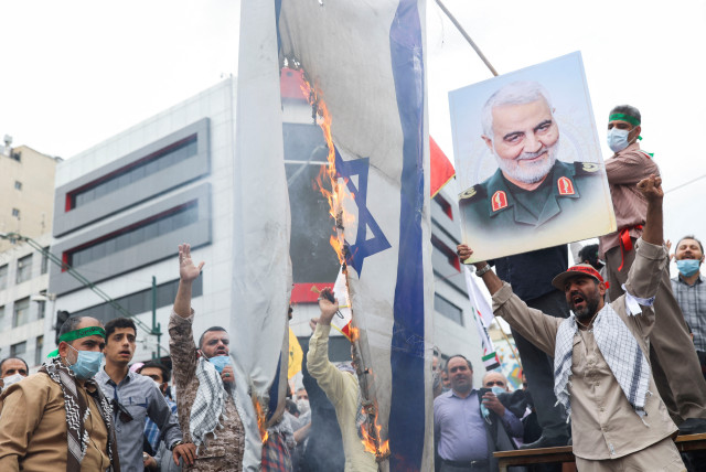 A man holds up a poster of the late Iranian Major-General Qassem Soleimani next to a burning Israeli flag as Iranians attend a rally marking the annual Quds Day, or Jerusalem Day, on the last Friday of the holy month of Ramadan in Tehran, Iran April 29, 2022 (credit: WANA NEWS AGENCY/REUTERS)