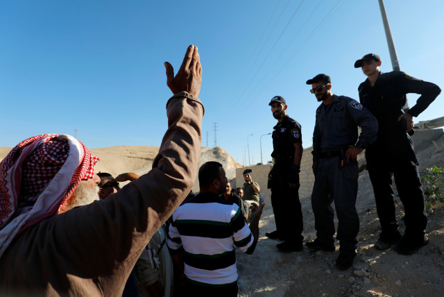  A Palestinian man gestures as Israeli policemen stand guard in the Bedouin village of Khan al-Ahmar that Israel plans to demolish, in the West Bank October 16, 2018. (credit: REUTERS/MOHAMAD TOROKMAN)