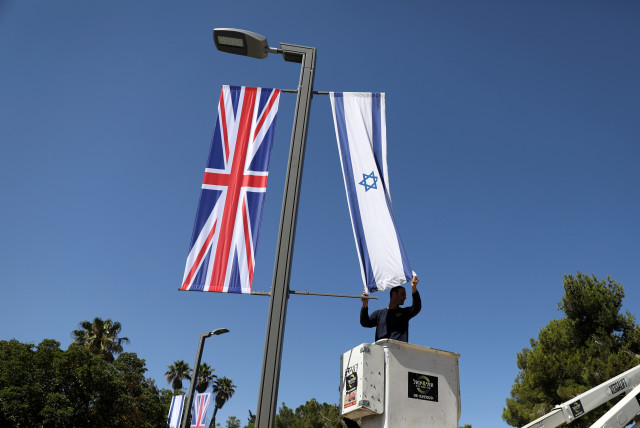 A Jerusalem municipality worker hangs an Israeli flag next to the British flag, the Union Jack, as he stands on a platform near Israel's presidential residence in Jerusalem ahead of the upcoming visit of Britain's Prince William, June 25, 2018 (photo credit: AMMAR AWAD/REUTERS)