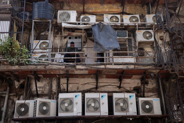  A man uses his mobile phone as he sits amidst the outer units of air conditioners, at the rear of a commercial building in New Delhi, India, April 30, 2022 (credit: ADNAN ABIDI/ REUTERS)