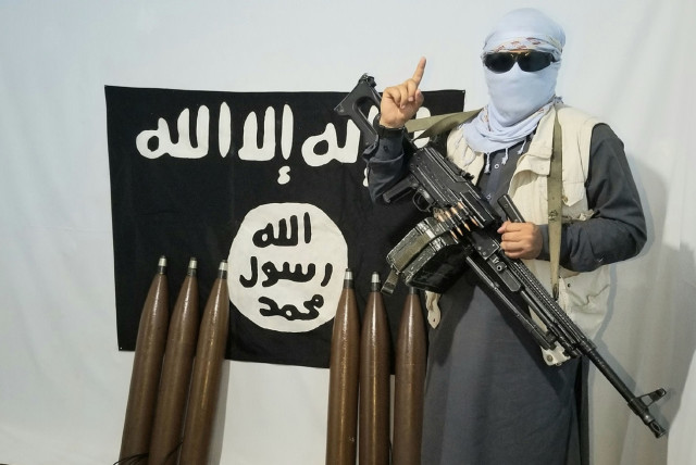  An ISIS fighter poses in front of an Islamic State flag (photo credit: Wikimedia Commons)
