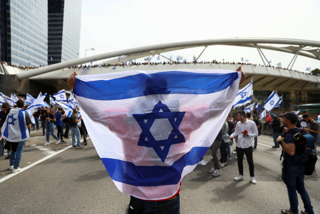  A demonstrator holds an Israeli flag as they attend the ''Day of Paralysis'' protest, as Israeli Prime Minister Benjamin Netanyahu's nationalist coalition government presses on with its judicial overhaul, in Tel Aviv, Israel March 23, 2023.  (credit: RONEN ZVULUN/REUTERS)