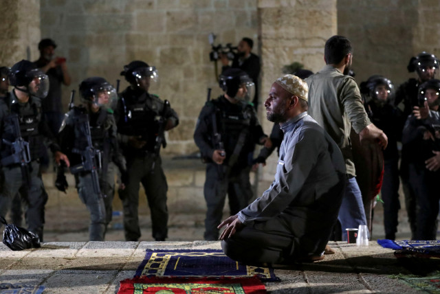  A Palestinian man prays as Israeli police gather during clashes at the compound that houses Al-Aqsa Mosque, known to Muslims as Noble Sanctuary and to Jews as Temple Mount. May 7, 2021. (credit: AMMAR AWAD/REUTERS)