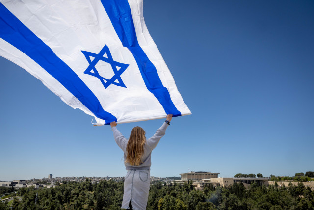 A woman waves a large Israeli flag as people watch the military airshow as part of Israel's 75th Independence Day celebrations, in Jerusalem, April 26, 2023.  (photo credit: YONATAN SINDEL/FLASH90)