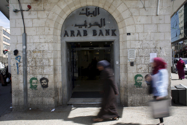  Palestinians walk past a bank in the West Bank city of Ramallah March 25, 2015.  (credit: REUTERS/MOHAMAD TOROKMAN)