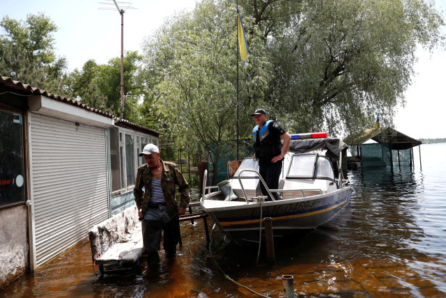 Mykola stands next to a police boat on a flooded island, which locals and officials say is caused by Russia's chaotic control of the Kakhovka dam downstream, amid Russia's attack on Ukraine, near Zaporizhzhia, Ukraine, May 20, 2023. (credit: BERNADETT SZABO / REUTERS)