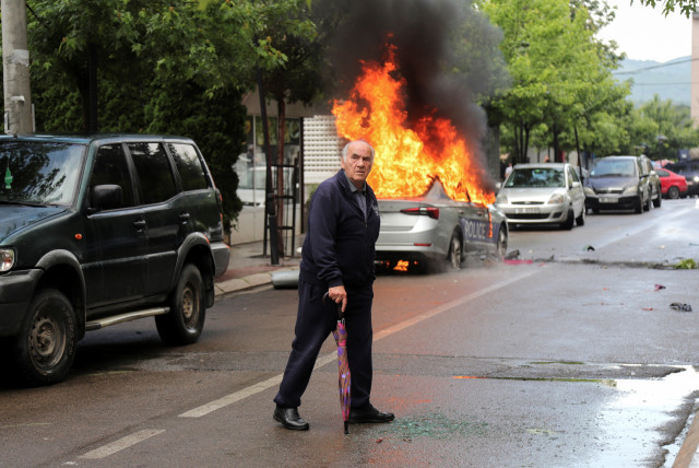 A man walks past a burning police car, during clashes between Kosovo police and ethnic Serb protesters, who tried to prevent a newly-elected ethnic Albanian mayor from entering his office, in the town of Zvecan, Kosovo, May 26, 2023 (credit: REUTERS/Miodrag Draskic)