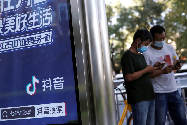  People wearing face masks use smartphones next to an advertisement of TikTok (Douyin) at a bus stop in Beijing, China August 24, 2020 (photo credit: REUTERS/TINGSHU WANG)