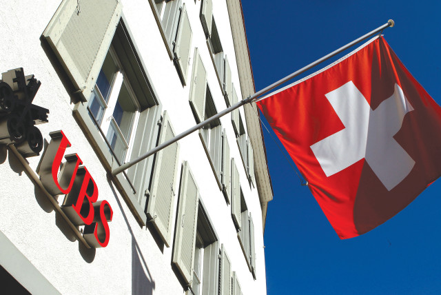  SWITZERLAND’S national flag is seen beside the logo of Swiss bank UBS, in front of a branch office in the town of Riehen, near Basel.  (photo credit: ARND WIEGMANN / REUTERS)
