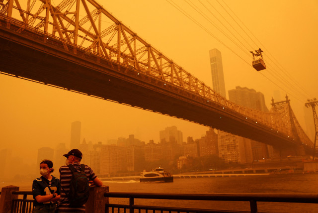  People wear protective masks as the Roosevelt Island Tram crosses the East River while haze and smoke from the Canadian wildfires shroud the Manhattan skyline in the Queens Borough New York City, US, June 7, 2023. (credit: Shannon Stapleton/Reuters)