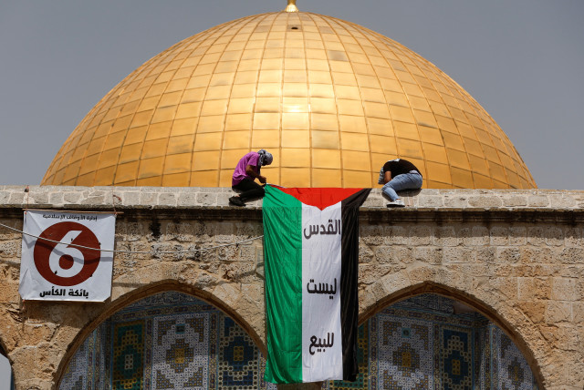  Palestinians mount a national flag in a protest on the last Friday of Ramadan ahead of the prayer in front of the Dome of the Rock, in the compound known to Muslims as Noble Sanctuary and to Jews as Temple Mount, in Jerusalem's Old City April 29, 2022. (credit: AMMAR AWAD/REUTERS)