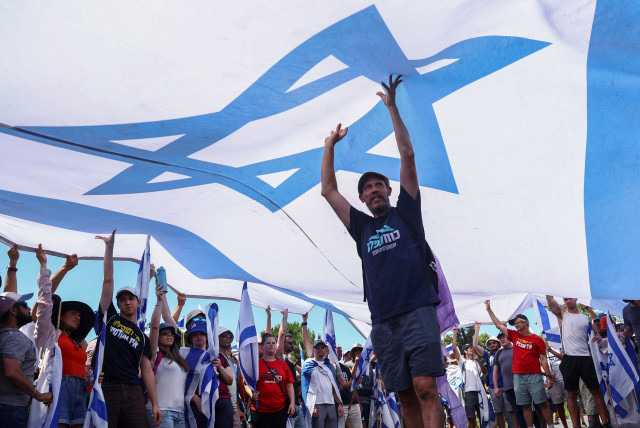  Protesters hold up a large Israeli flag at a demonstration following a parliament vote on a contested bill that limits Supreme Court powers to void some government decisions, in Jerusalem July 24, 2023. (credit: REUTERS/Ronen Zvulun)
