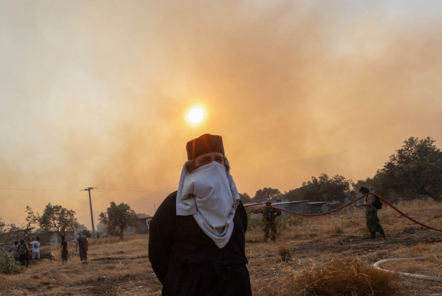  A Greek Orthodox priest covers his face to protect from smoke as firefighters, volunteers and police officers prepare to tackle a wildfire approaching the village of Masari, on the island of Rhodes, Greece, July 24, 2023. (credit: REUTERS/Nicolas Economou)