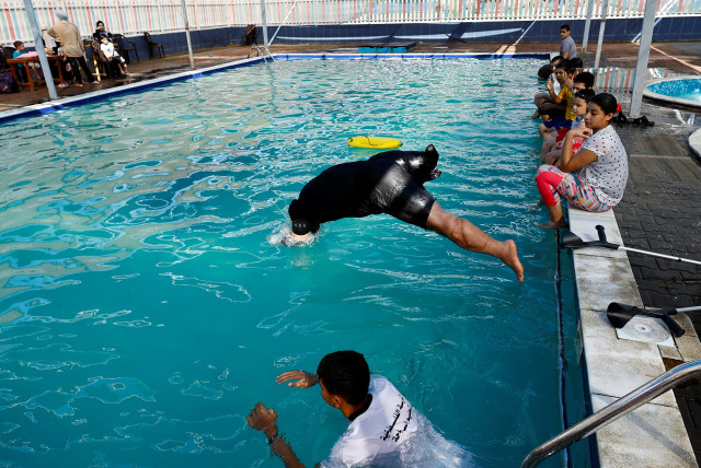  Majdi El-Tattar, a man with disability from Gaza trains children to swim as he became a high-in-demand swimming coach, in Gaza City August 5, 2023 (credit: REUTERS/IBRAHEEM ABU MUSTAFA)