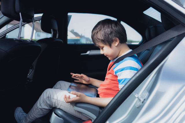  A young child uses a tablet in the back seat of a car (illustrative) (credit: INGIMAGE)