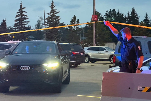  A police officer holds up crime scene tape to allow people to leave after a shooting incident at the West Edmonton Mall in Edmonton, Alberta, Canada August 21, 2023. (credit: REUTERS)