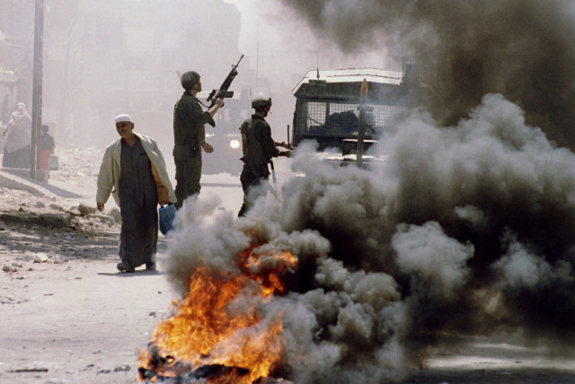  An elderly Palestinian man calmy walks past Israeli Border Police and burning tires in the Shatti refugee camp in the Gaza Strip. April 22, 1993 (credit: REUTERS)
