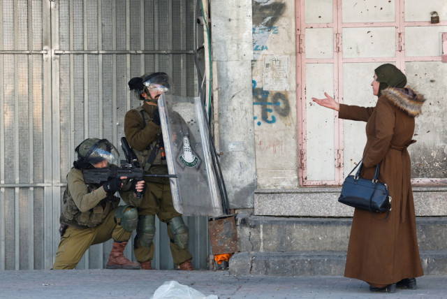  A Palestinian woman gestures in front of Israeli troops during a protest over the killing of three Palestinian gunmen by Israeli forces, in Hebron in the Israeli-occupied West Bank, February 9, 2022. (credit: MUSSA QAWASMA / REUTERS)