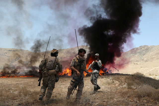  Afghan police officers chat with each others in front of a pile of burning illegal drugs in the outskirts of Kabul, Afghanistan July 1, 2021. (credit: REUTERS/OMAR SOBHANI)