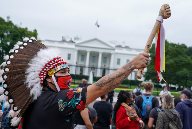  A demonstrator wears a traditional Native American headdress during an Indigenous Peoples' Day protest outside of the White House in Washington, U.S., October 11, 2021. (credit: REUTERS/SARAH SILBIGER)