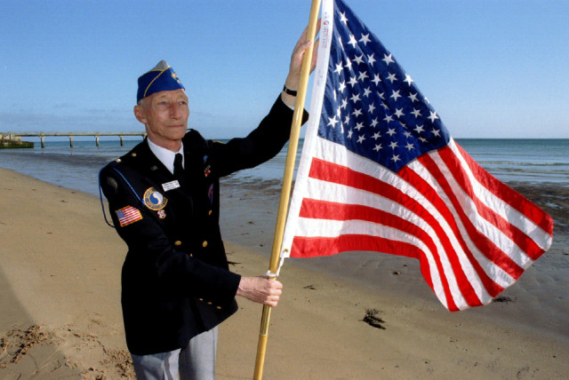 Dutch WWII veteran Robert Wynoogst, 68, who landed in Normandy with the US 29th infantry division on 6th June1944, plants an American flag in the sand on Omaha Beach, June3 (credit: REUTERS)