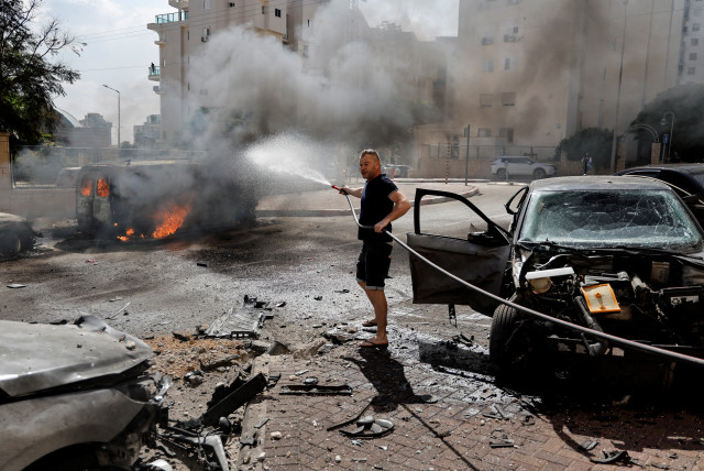  A man works to put out a fire engulfing a van, as rockets are launched from the Gaza Strip, in Ashkelon, southern Israel October 7, 2023. (credit: REUTERS/AMMAR AWAD)