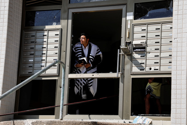  A man wearing a Jewish prayer shawl looks out of the damaged entranceway to a building, as rockets are launched from the Gaza Strip, in Ashkelon, southern Israel October 7, 2023. (credit: REUTERS/AMMAR AWAD)