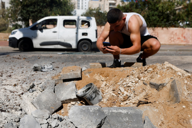  A man photographs a remnant of a rocket launched from Gaza that is lying on the ground, in Ashkelon (credit: AMIR COHEN/REUTERS)