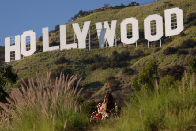 A woman poses by the iconic Hollywood sign on the day members of the Writers Guild of America (WGA) approved a new three-year contract with major studios, in Los Angeles, California, U.S., October 9, 2023. (credit: MARIO ANZUONI/REUTERS)