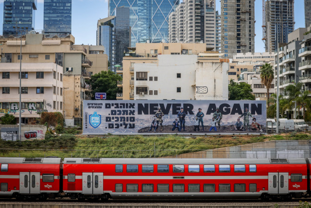  A large billboard with the words ''Never Again'' above the Ayalon highway in Tel Aviv, October 18, 2023. (credit: Chaim Goldberg/Flash90)
