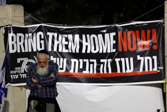  A man stands next to a banner as hostages are expected to be released by the Palestinian militant group Hamas, amid a hostages-prisoners swap deal between Hamas and Israel, in Tel Aviv, Israel, November 26, 2023 (credit: REUTERS/ATHIT PERAWONGMETHA)