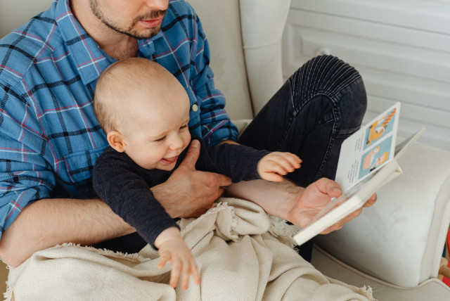  Father reading to a baby boy. (credit: PEXELS)