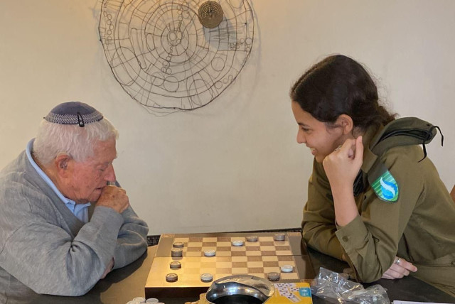  Education and Youth Corps member Gaya Barkan plays checkers with evacuee Yaakov. (credit: IDF SPOKESPERSON UNIT)