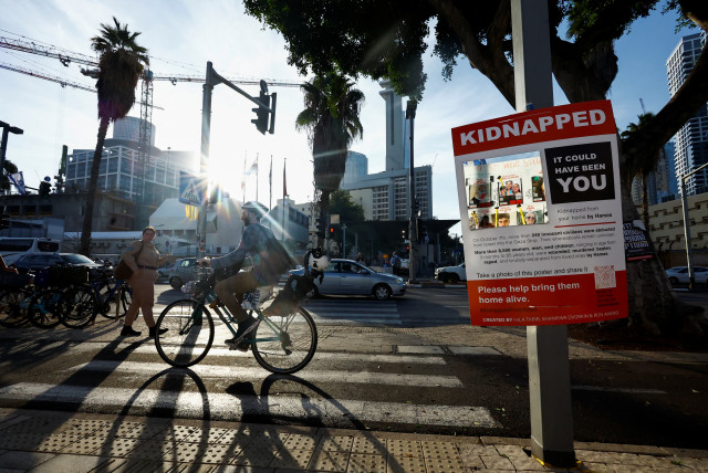 A man cycles past a poster with a mirror reflecting the message board with pictures of hostages, who are being held in the Gaza Strip after they were seized by Hamas gunmen on October 7, in Tel Aviv, Israel December 7, 2023.  (credit: REUTERS/CLODAGH KILCOYNE)