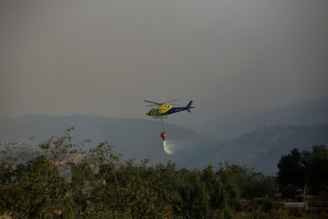  A helicopter flying over a burnt area drops water from a bucket to douse flames during the spread of wildfires in Vina del Mar, Chile February 3, 2024. (credit: REUTERS/SOFIA YANJARI)