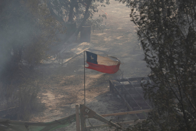  Chile's national flag flies amidst smoke and near the burnt remains of a house following the spread of wildfires, in Vina del Mar, Chile February 3, 2024. (credit: REUTERS/SOFIA YANJARI)