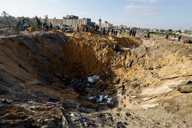 Palestinians gather near a crater at the site of an Israeli strike on a house in Rafah, in the southern Gaza Strip, February 18, 2024 (credit: REUTERS/MOHAMMED SALEM)